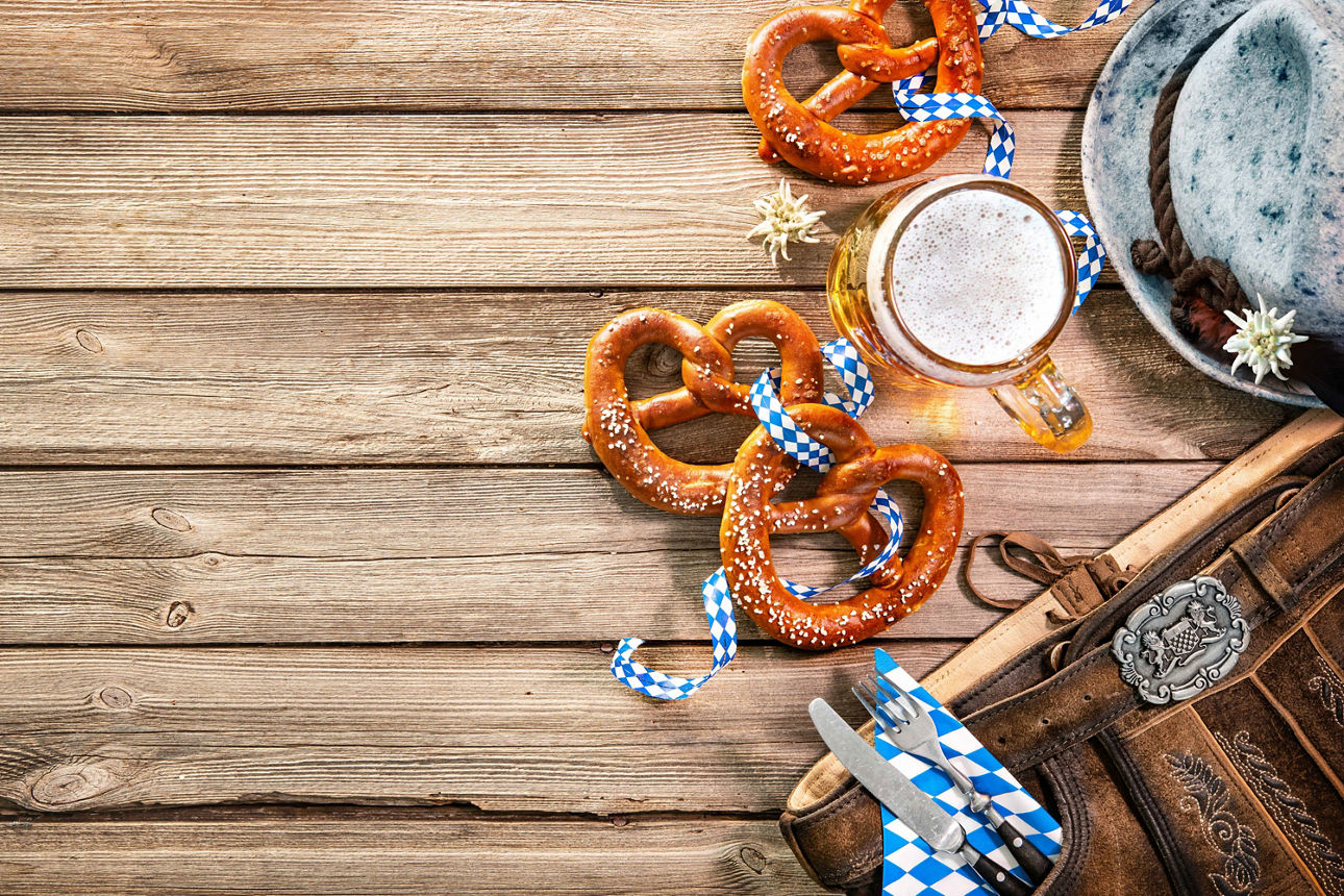 Oktoberfest-Arrangement mit Brezeln, Maßkrug, Trachtenhut und Lederhose auf Holztisch