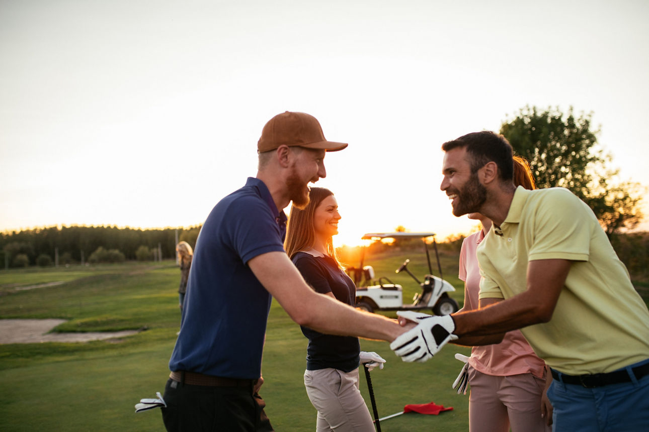 2 Paare begrüßen sich im Golf-Outfit auf einem Golfplatz
