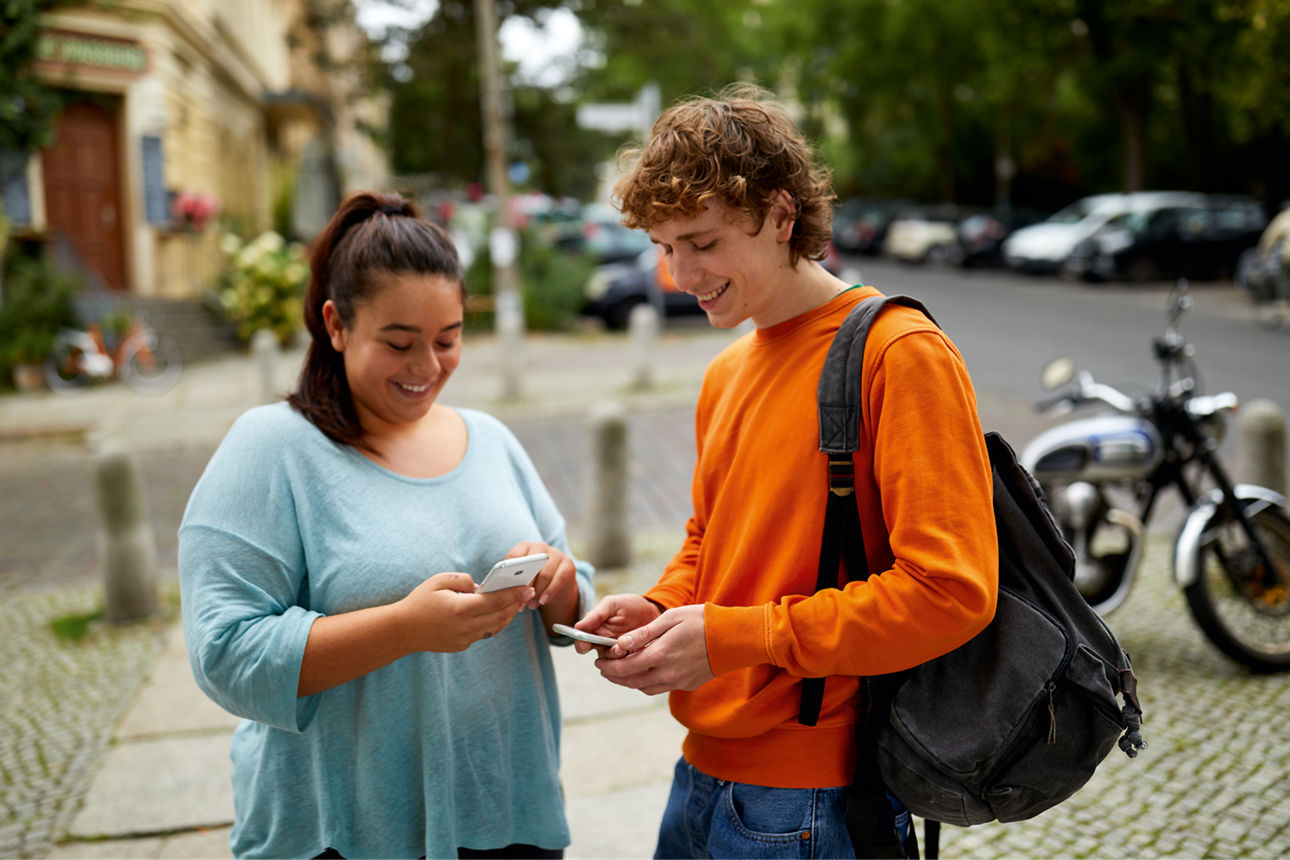 Zwei Jugendliche stehen auf der Straße und schauen jeweils auf ihr Smartphone.