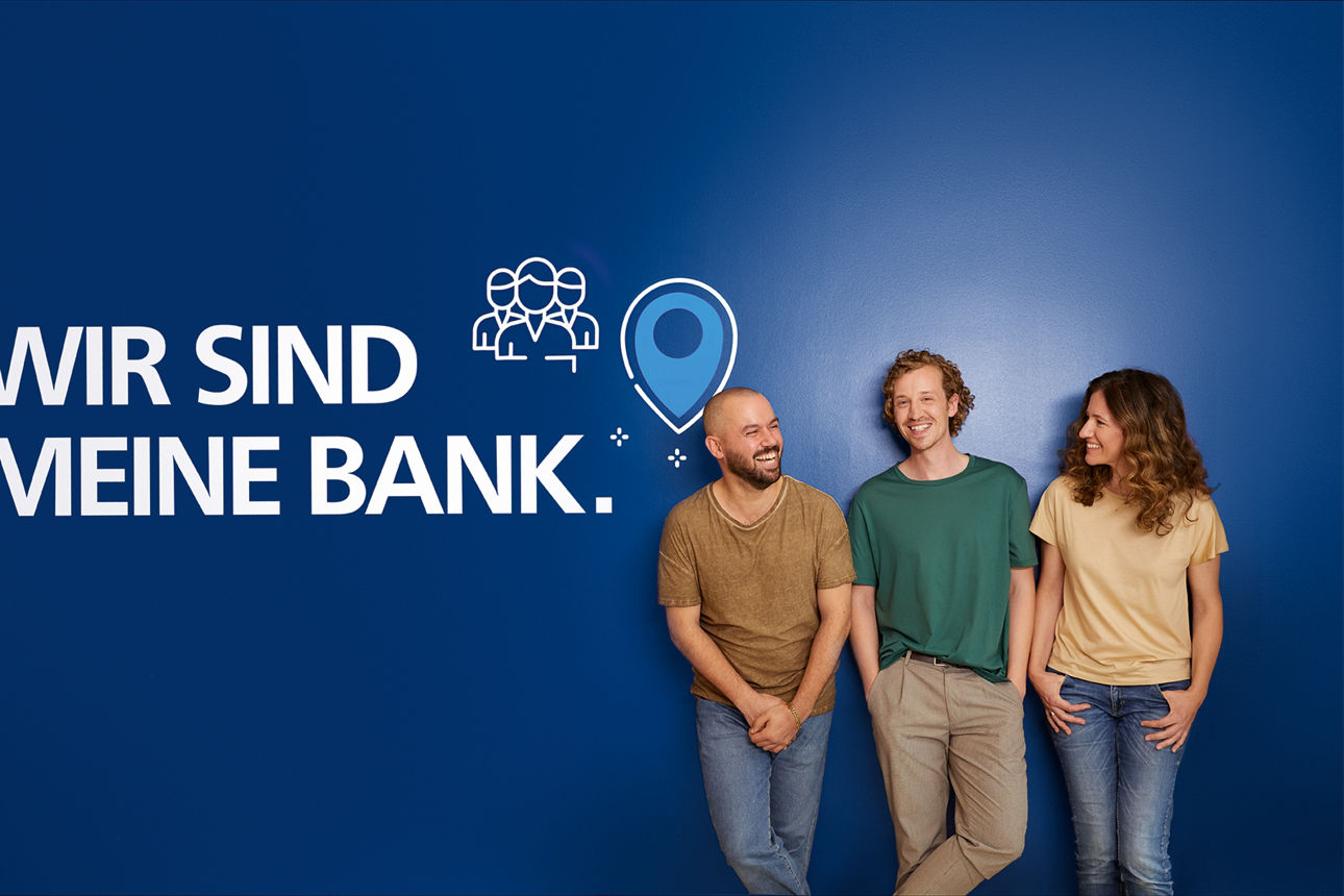 Gruppe von 3 Personen an blauer Wand mit Aufschrift "Wir sind meine Bank"