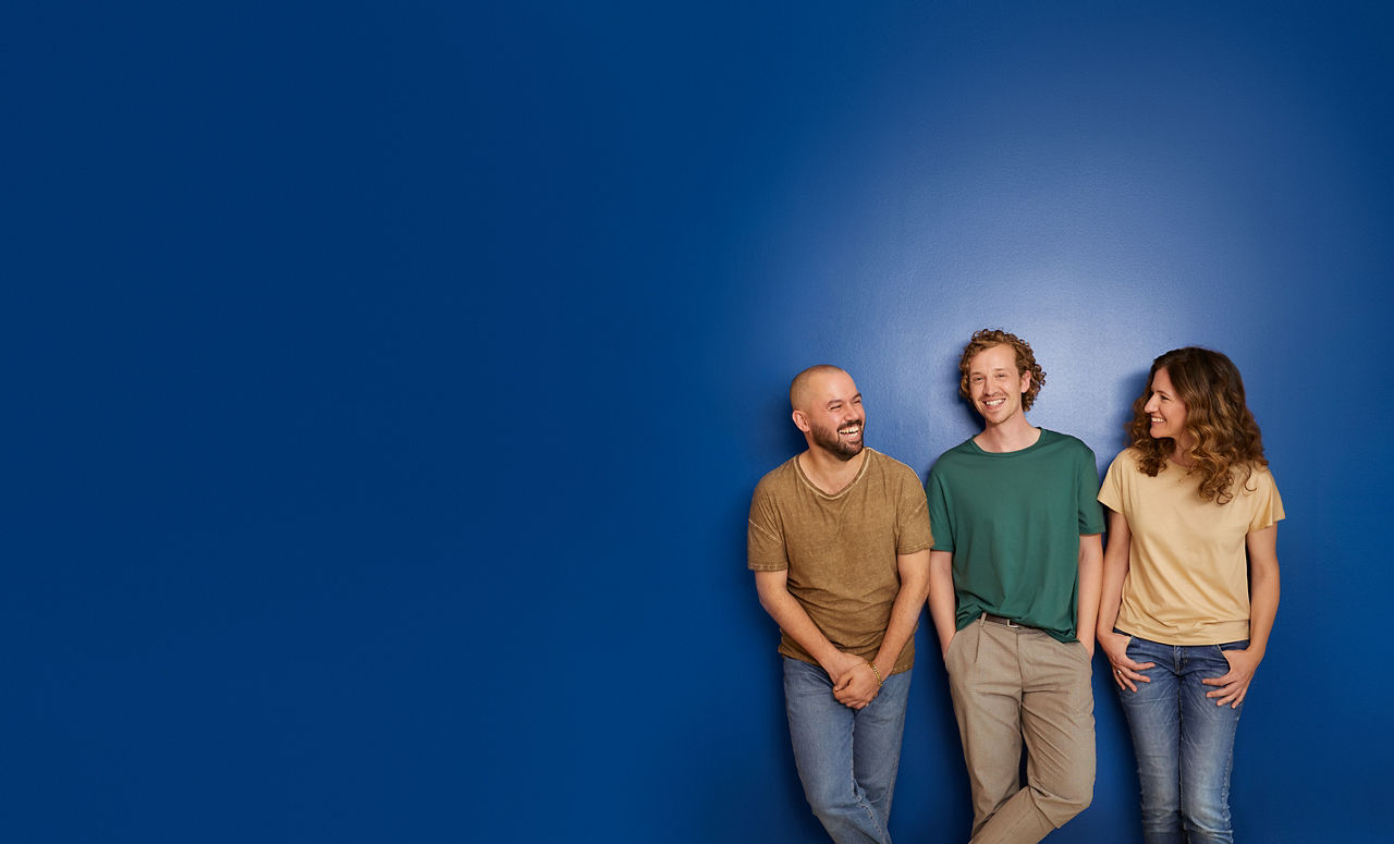 Zwei Männer und eine Frau vor einer blauen Wand am lachen.