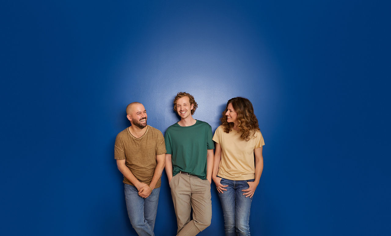 Drei lachende Menschen stehen vor einer blauen Wand