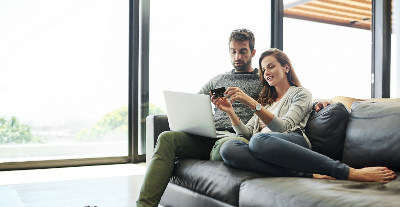 Ein Mann und eine Frau liegen auf dem Sofa und halten einen Laptop und eine Kreditkarte in der Hand