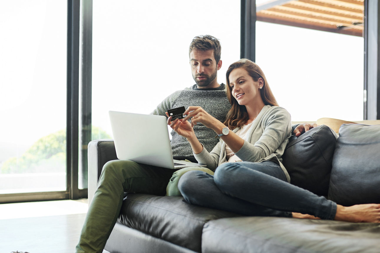 Ein Mann und eine Frau liegen auf dem Sofa und halten einen Laptop und eine Kreditkarte in der Hand