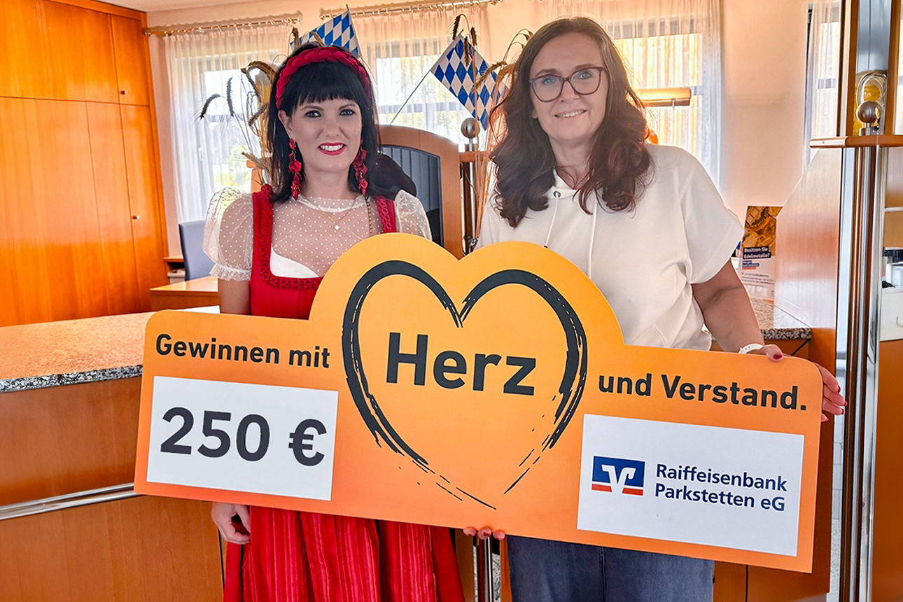 Zwei Frauen, die ein Werbeschild für ein Gewinnspiel der Raiffeisenbank Parkstetten eG in der Hand halten.