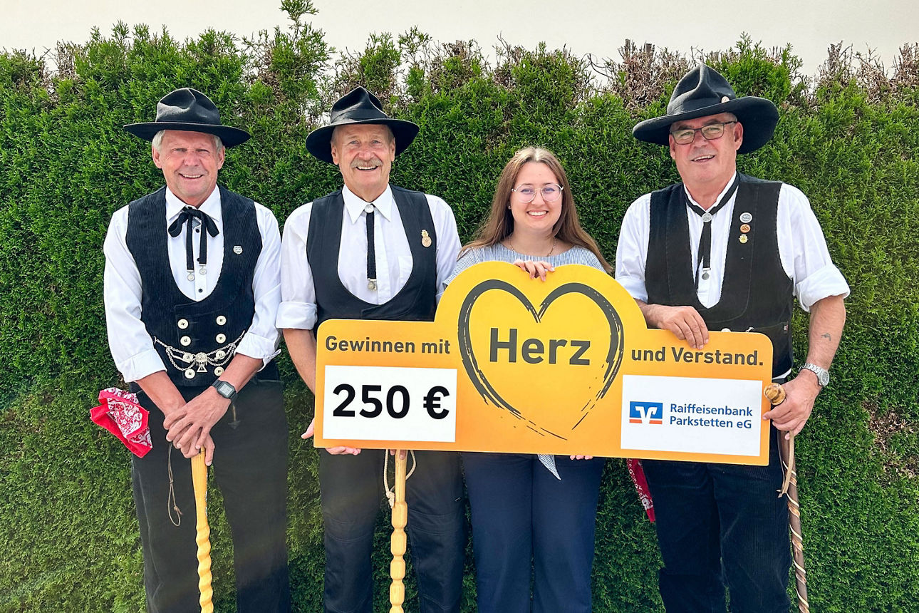 Vier Personen, davon drei in Zimmermannskluft, präsentieren Spendenscheck über 250 Euro und Herzschild