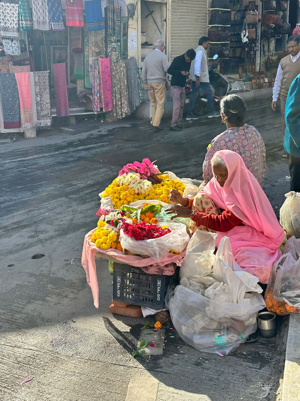Eine Frau steht an einem Marktstand und verkauft eine Vielzahl bunter Blumen an vorbeigehende Kunden