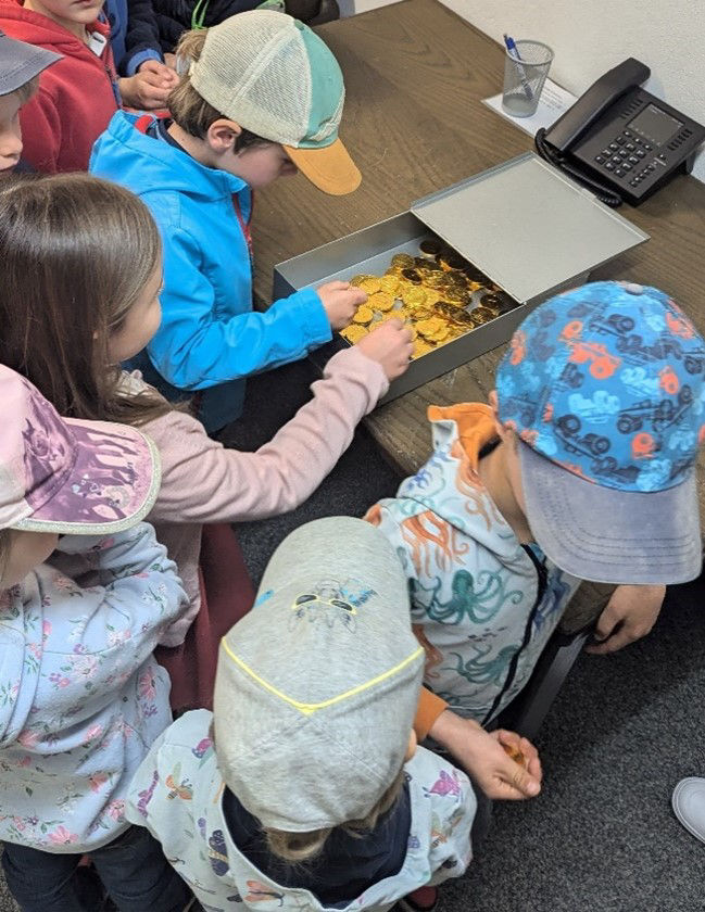Kleine Kinder untersuchen gespannt eine Schachtel voller Goldmünzen.