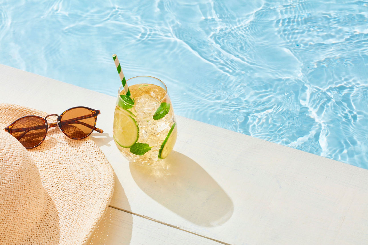 Sonnenhut, Sonnenbrille und Sommergetränk an einem Pool