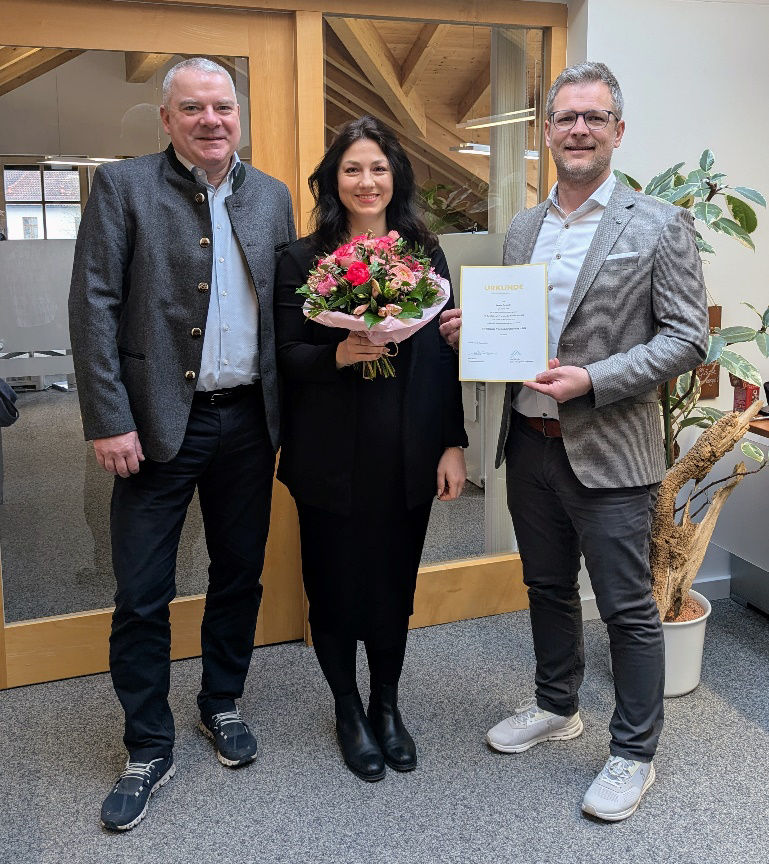 Drei Personen, mittig mit Blumenstrauß, rechts mit Zertifikat zur Vorstandsreferentin