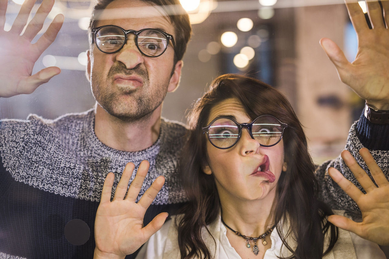 Zwei Personen mit Brillen kleben mit den Gesichtern an einer Glasscheibe