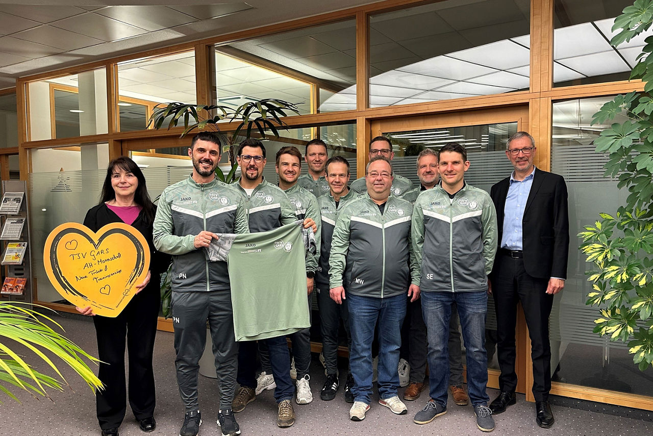 eine Gruppe an Menschen in Trainingsanzügen, ein Mann hält ein Trikot hoch