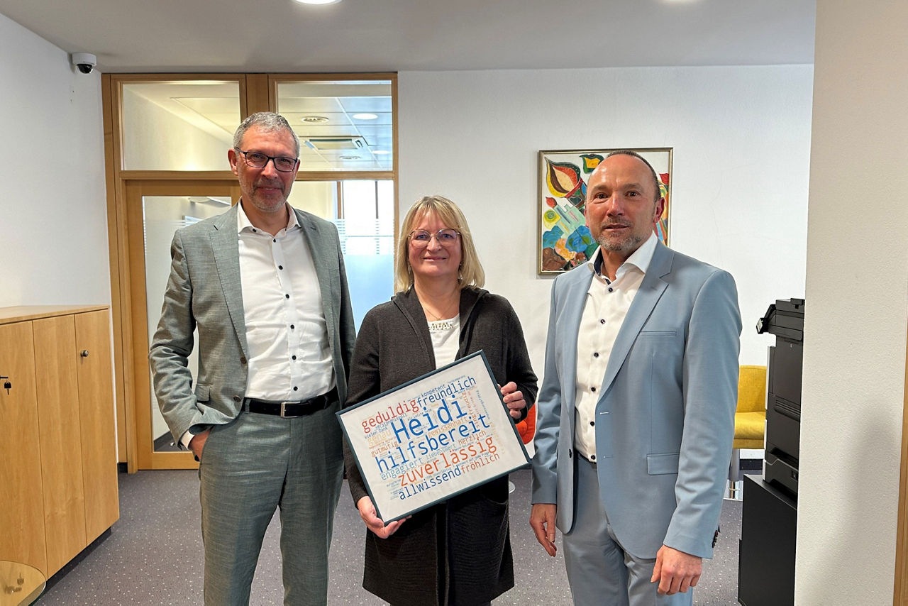 zwei Männer flankieren eine lächelnde Frau, die ein Bild in der Hand hält