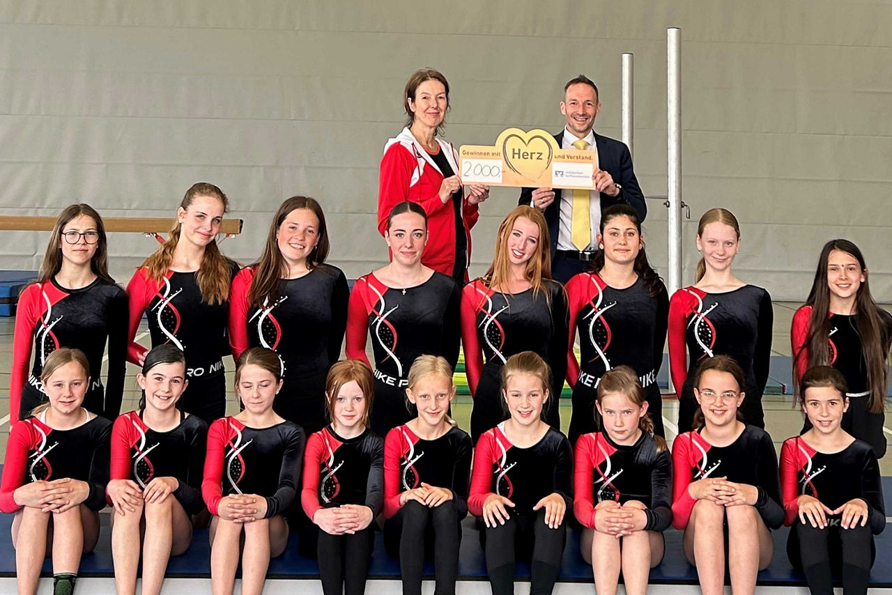 Eine große Gruppe junger Turnerinnen posiert in einer Sporthalle in mehreren Reihen