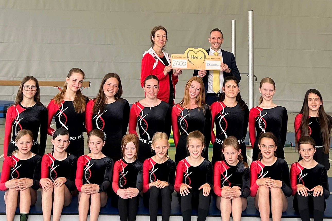 Eine große Gruppe junger Turnerinnen posiert in einer Sporthalle in mehreren Reihen