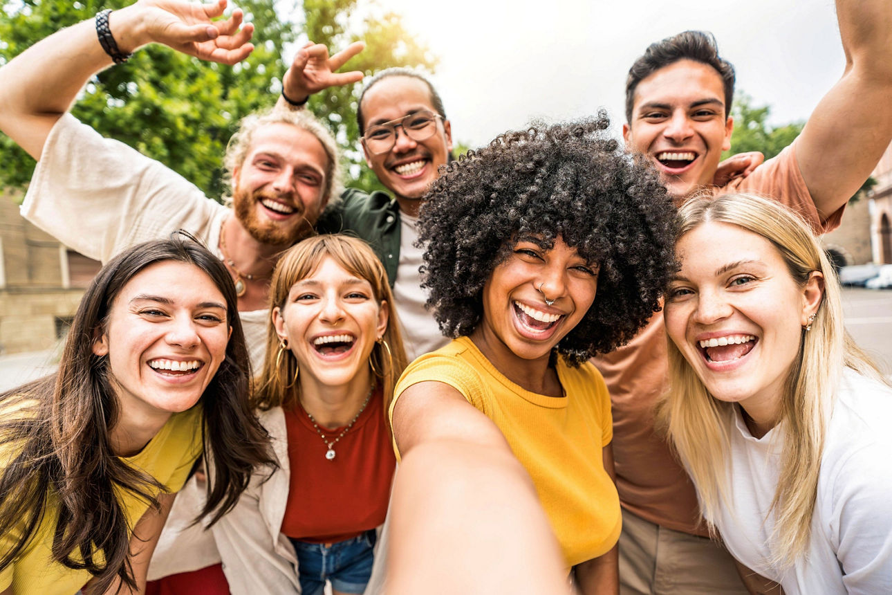 Sieben junge Menschen machen ein Selfie und lachen dabei in die Kamera