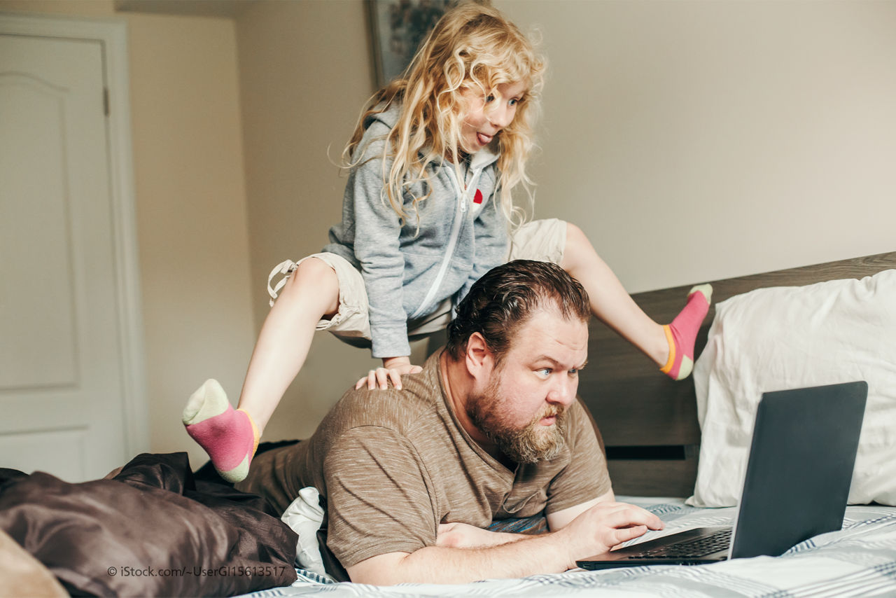 Kind springt über den Rücken des am Laptop arbeitenden Vaters.