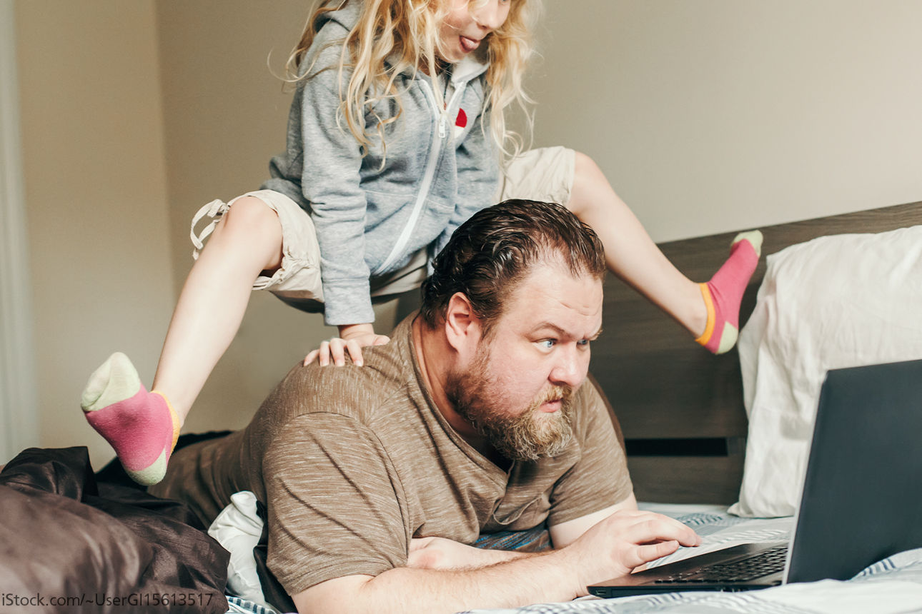 Kind springt über den Rücken des am Laptop arbeitenden Vaters.