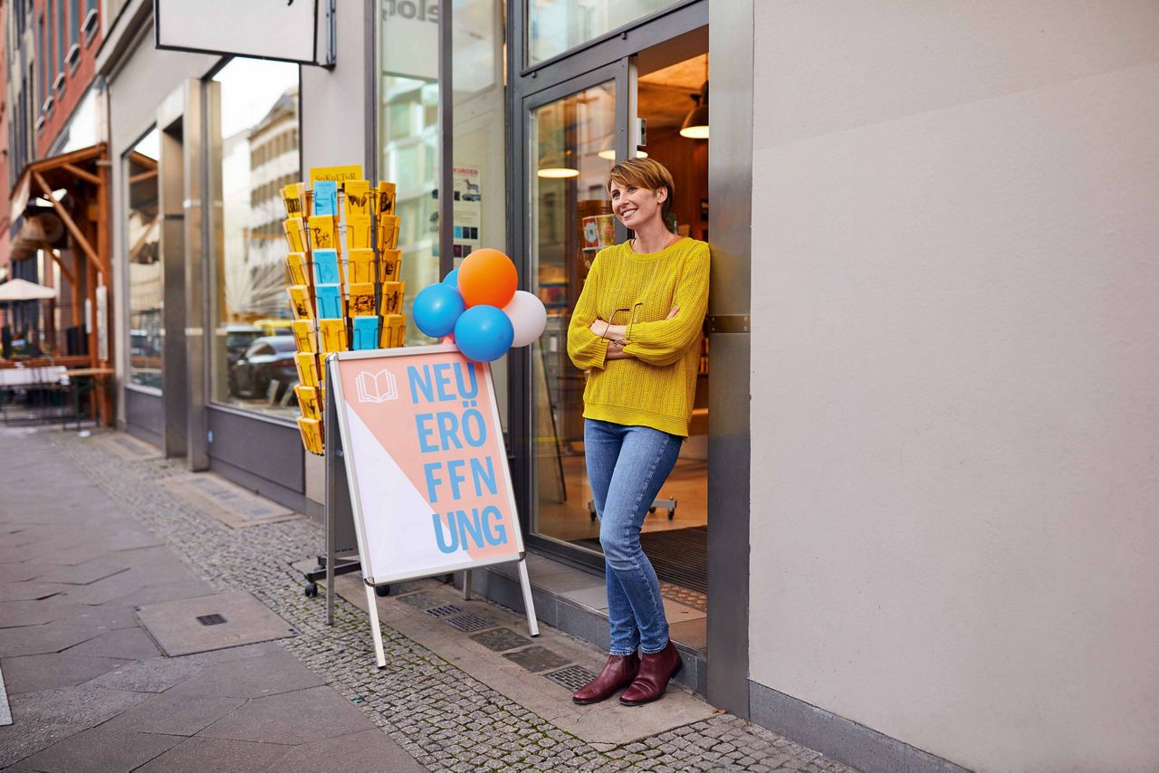 Frau steht lächelnd vor ihrem neu eröffneten Laden