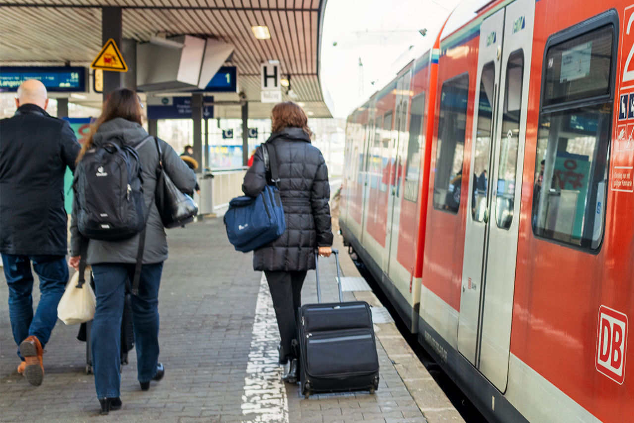 Reisende mit Koffern vor einem stehenden Zug am Bahnsteig