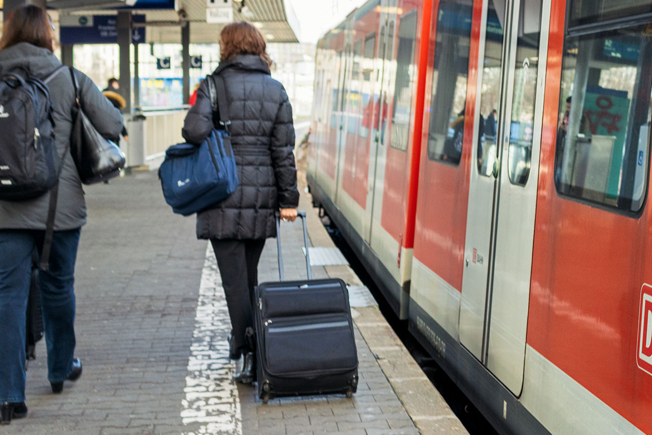 Reisende mit Koffern vor einem stehenden Zug am Bahnsteig