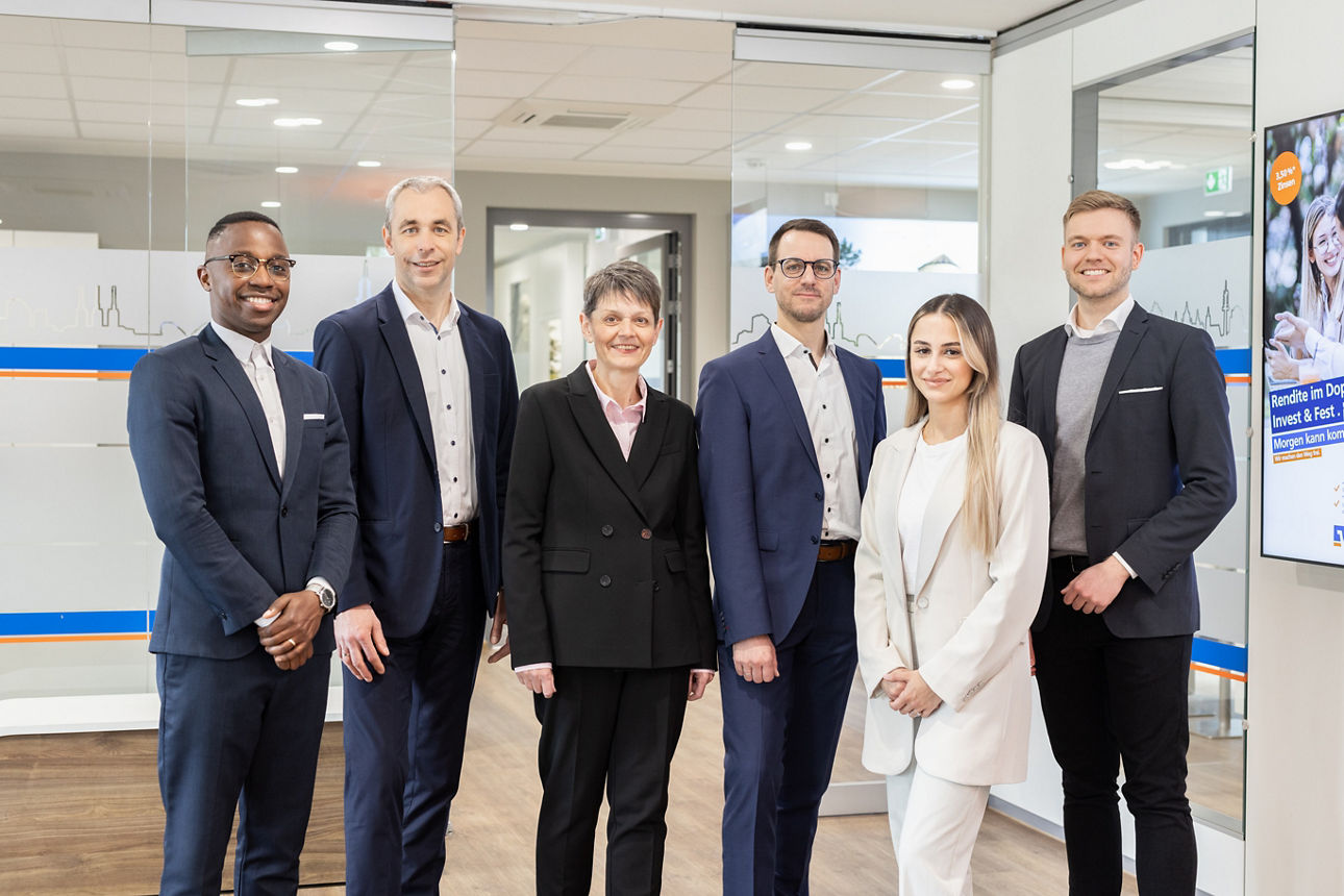 Mitarbeitende der Hannoverschen Volksbank stehen im Büroraum und lächeln