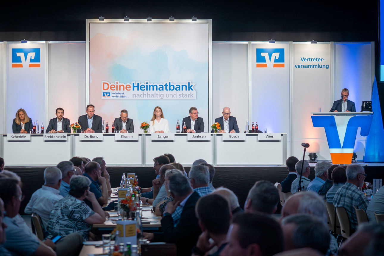 Vorstand und Aufsichtsrat der Volksbank an der Niers sitzen auf der Bühne der Vertreterversammlung