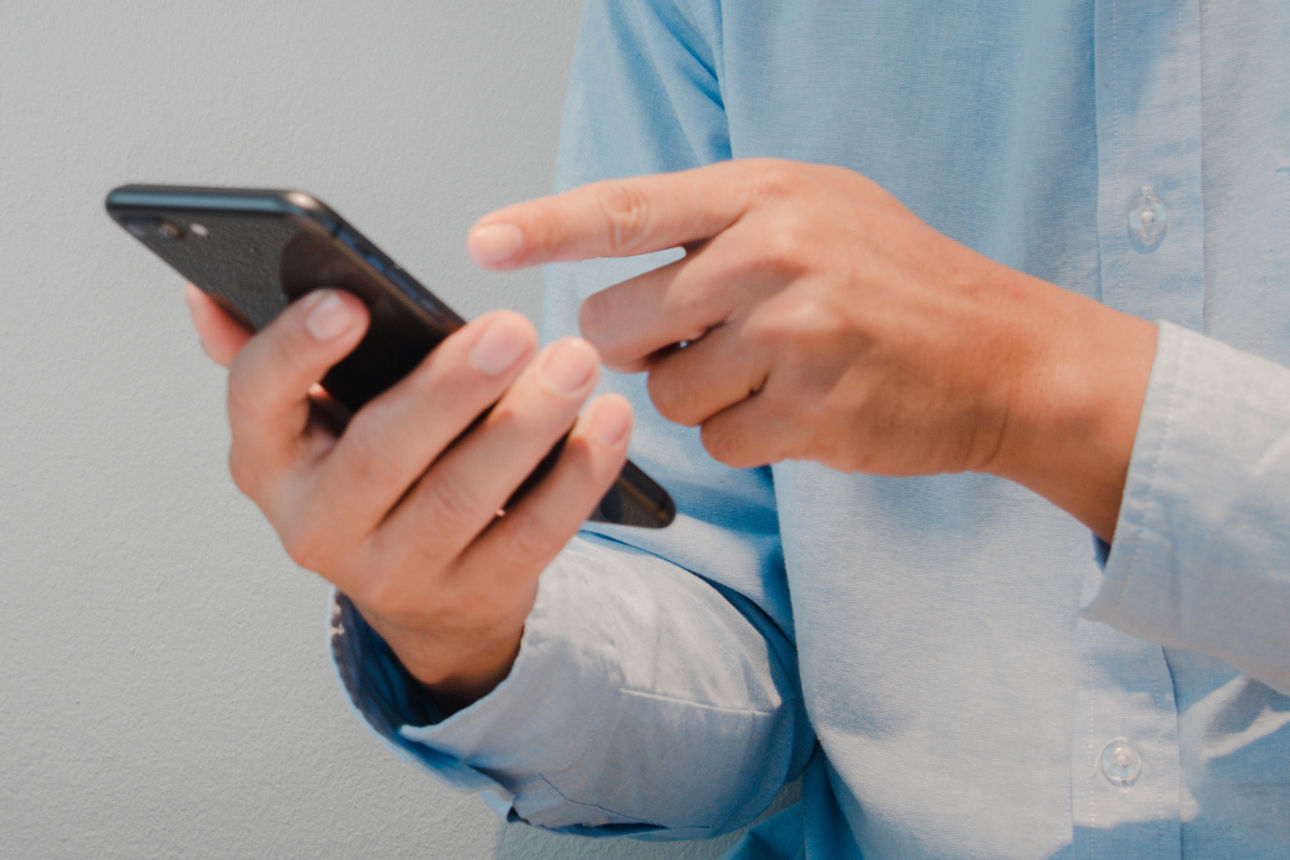 Eine Person tippt auf ein Smartphone, daneben ist ein großes Paragrafenzeichen als Symbol für Recht.