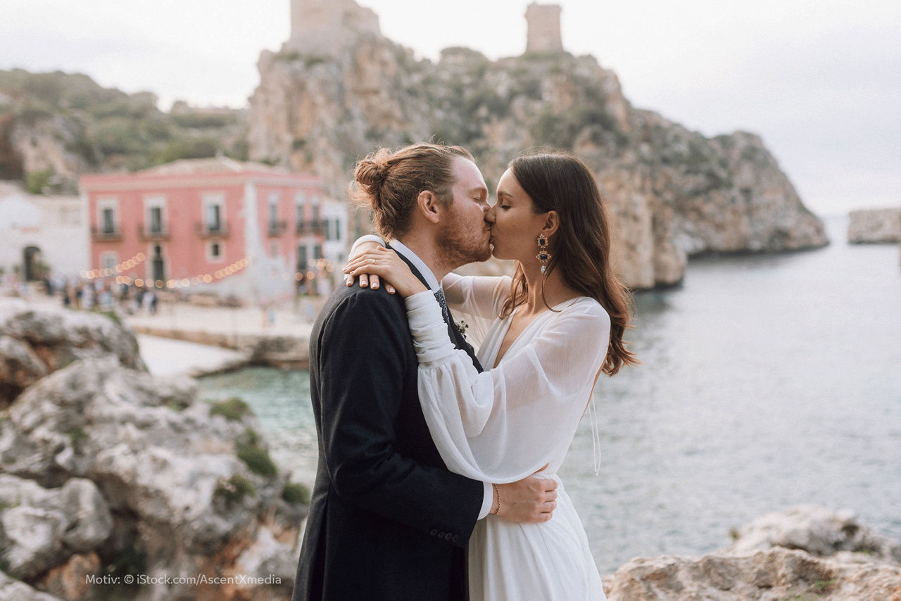 Hochzeitspaar küsst sich vor Steilküste in mediterraner Kulisse.