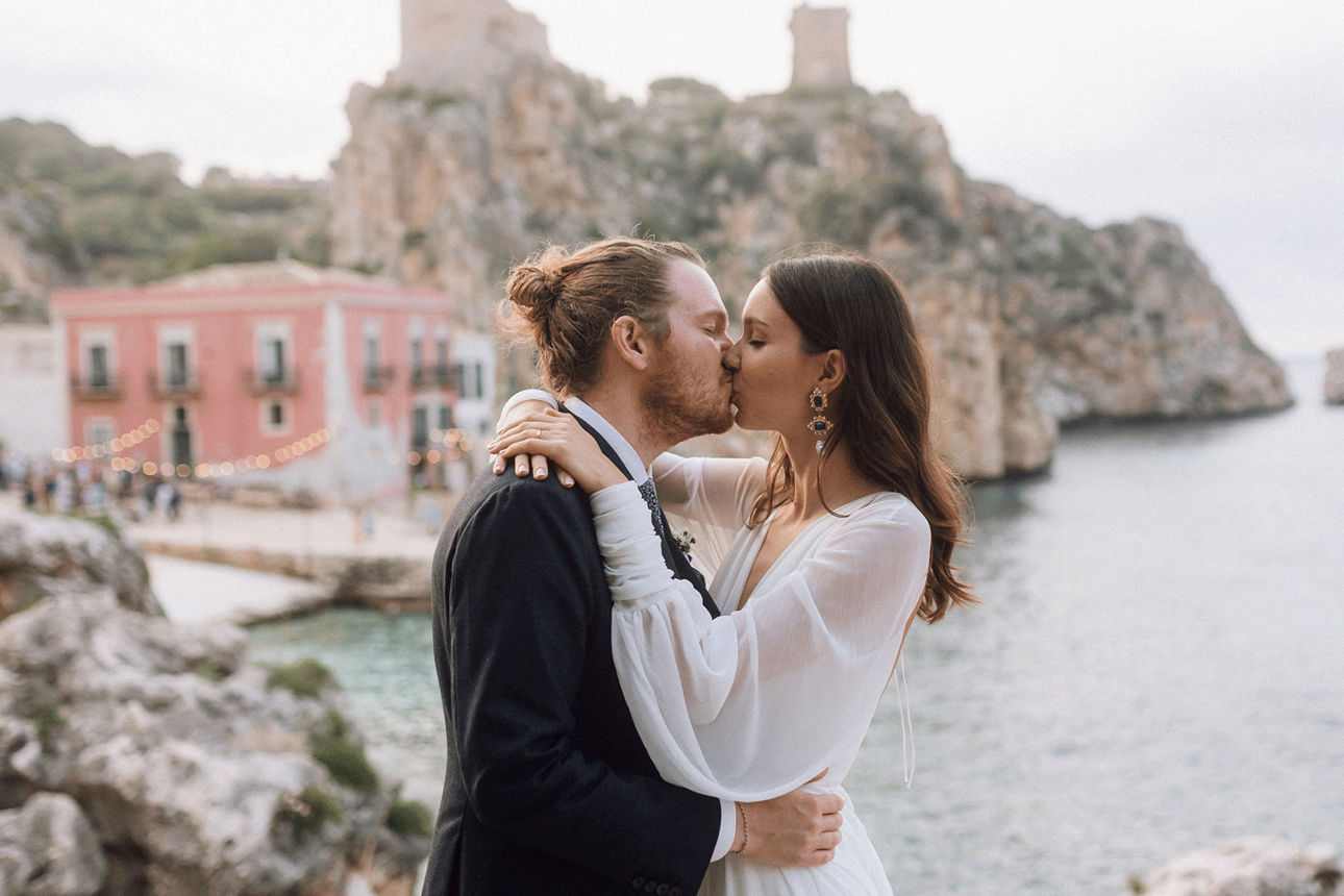 Hochzeitspaar küsst sich vor Steilküste in mediterraner Kulisse.