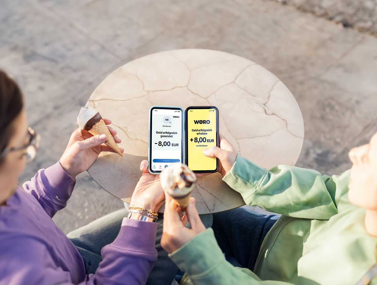Zwei Personen halten ihr Smartphone in der Hand und verschicken Geld über wero