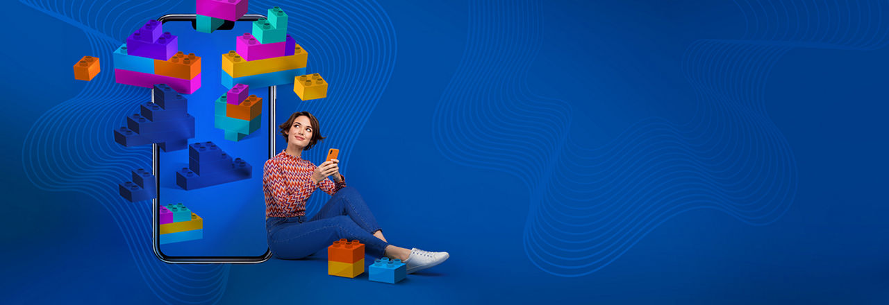 Junge Frau mit Handy in der Hand vor einem blauen Hintergrund und schwebenden Bauklötzen