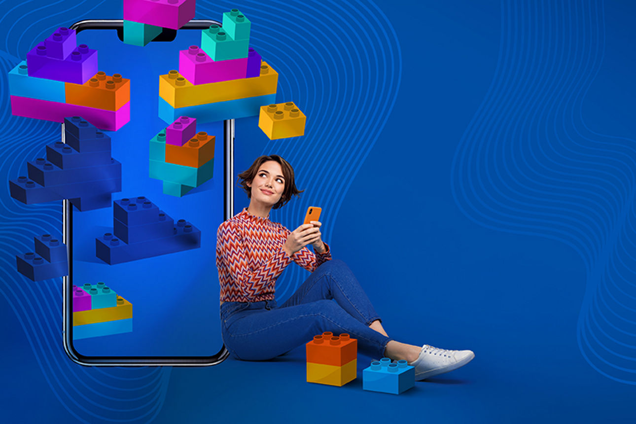 Junge Frau mit Handy in der Hand vor einem blauen Hintergrund und schwebenden Bauklötzen