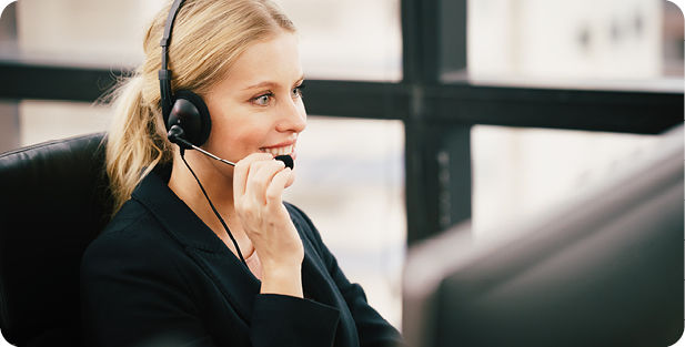 Eine Frau sitzt vor dem Schreibtisch mit einem Headset und telefoniert