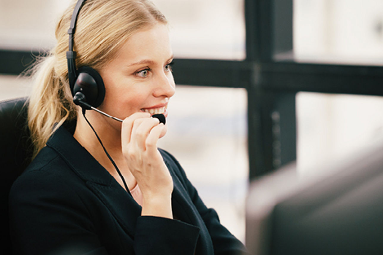 Eine Frau sitzt vor dem Schreibtisch mit einem Headset und telefoniert
