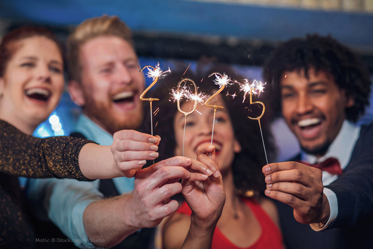 Vier lachende Menschen halten je eine Ziffer einer Wunderkerze für 2025 hoch.