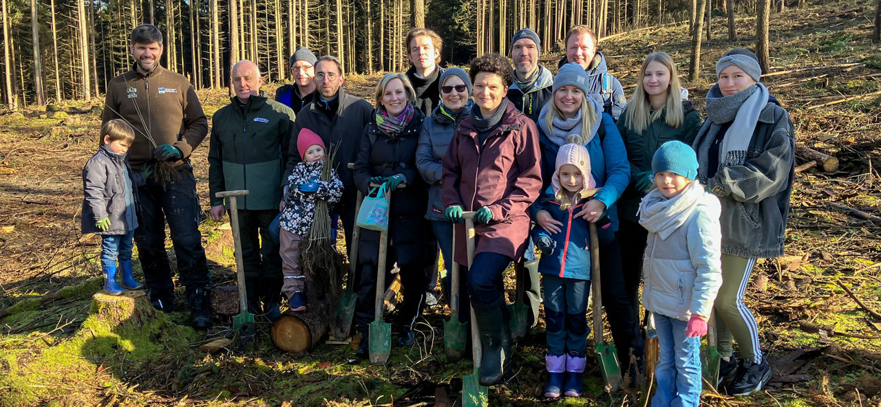 Mitarbeiter der Sparda-Bank und Familien stehen in einem Wald und pflanzen Bäume in Bamberg