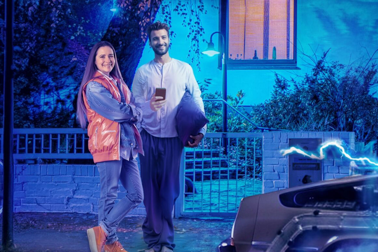 Frau und Mann stehen vor Haus, ein schnelles Auto fährt weg