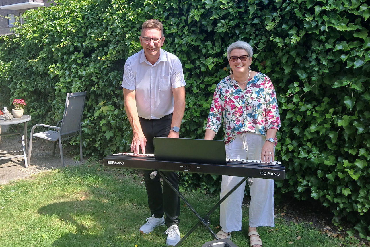 Ein Mitarbeiter der Volksbank und eine Frau vor einer Hecke mit einem e-Piano und einer Box 