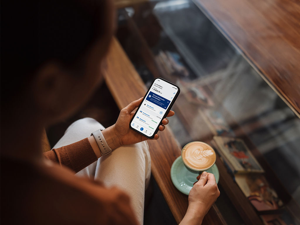 Frau mit Café und ein Handy mit der VR Banking App in der Hand