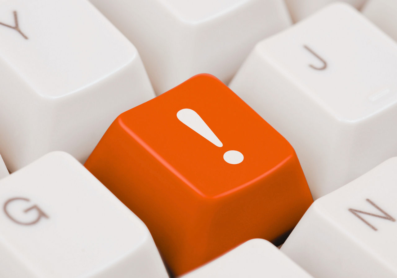 Eine orangefarbene Taste mit weißem Ausrufezeichen befindet sich zwischen weißen Tastaturtasten.
