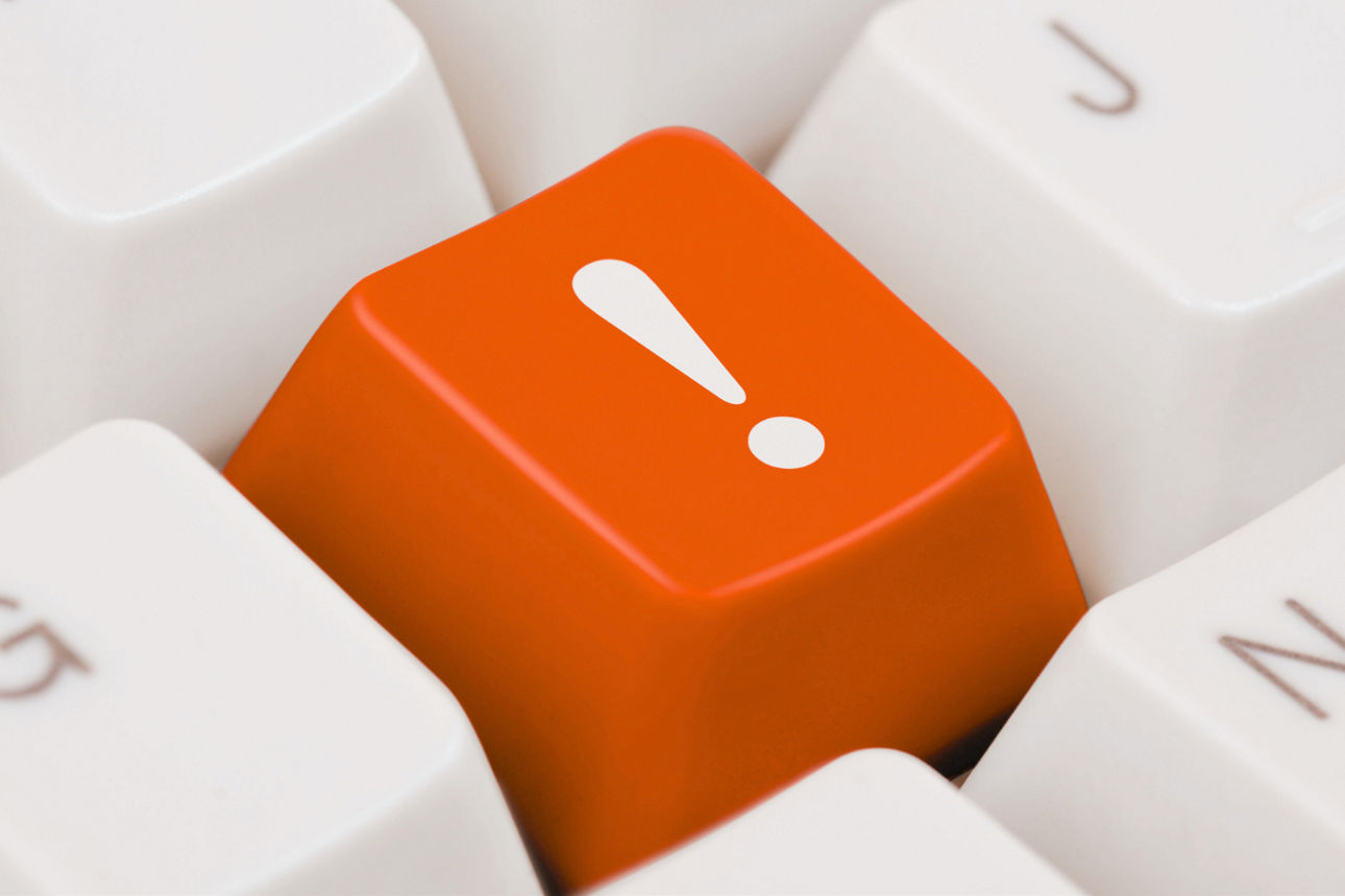 Eine orangefarbene Taste mit weißem Ausrufezeichen befindet sich zwischen weißen Tastaturtasten.