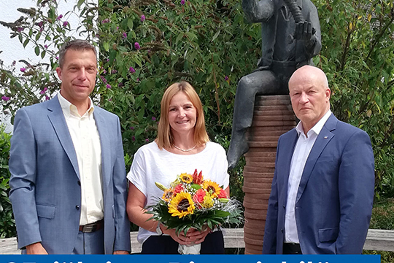 Zwei elegant gekleidete Männer und eine Frau halten einen Blumenstrauß 