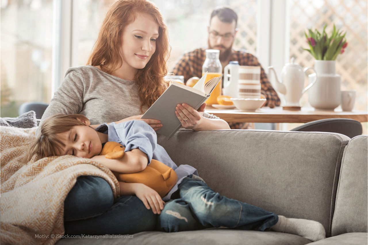 Kind kuschelt sich in den Schoß seiner Mutter, während sie ein Buch liest.