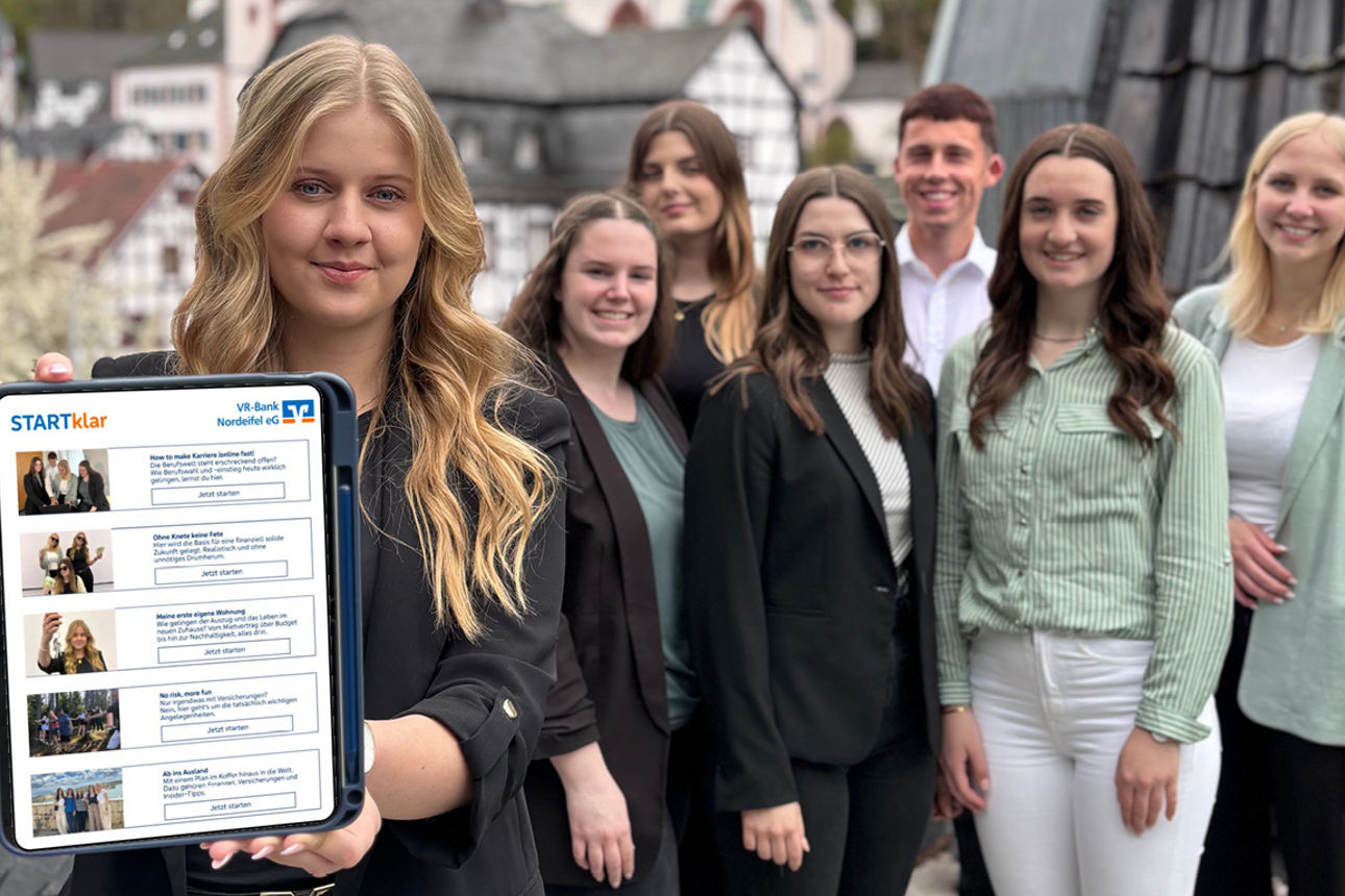 Azubis stehen zusammen wähend ein Azubi ein Tablet in die Kamera hält