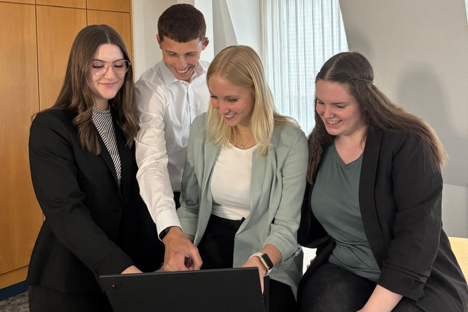 Mehrere Personen stehen nebeneinander und schauen auf einen Laptop