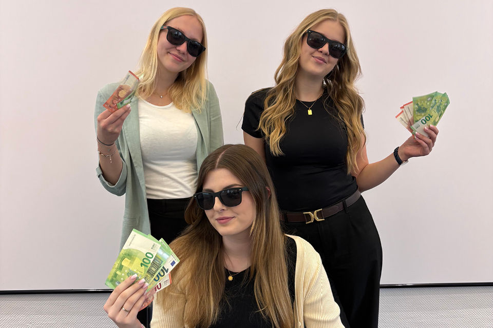 Drei Frauen tragen Sonnenbrillen und halten Geldscheine in der Hand