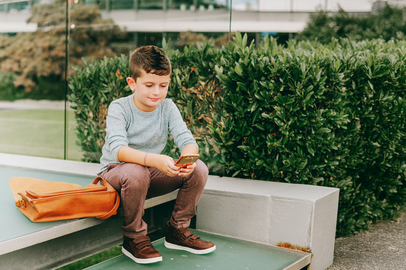 ein Junge sitzt auf einer Bank und spielt auf seinem Handy