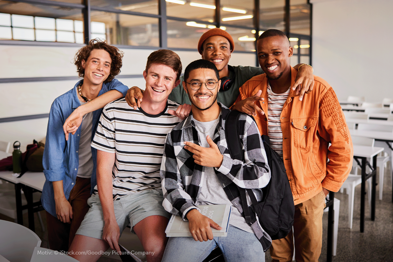 5 junge Männer unterschiedlicher Herkunft stehen als Gruppe in einem Klassenraum.