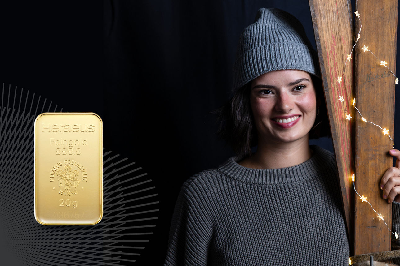 Eine Frau mit Mütze die zwei alte Skier hält. Neben ihr ein Goldbarren.